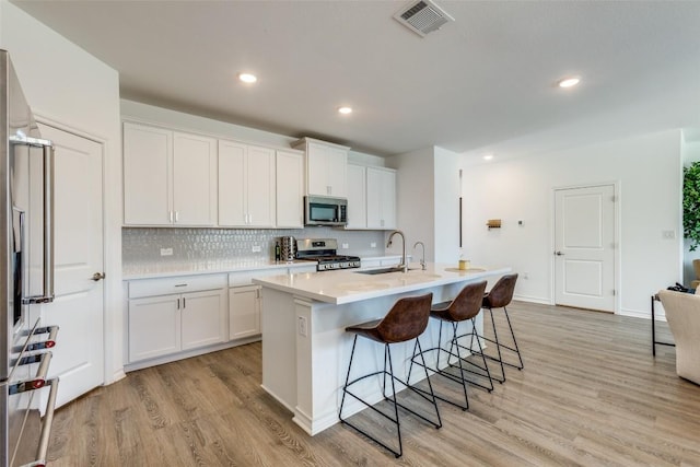 kitchen with a sink, light wood-type flooring, appliances with stainless steel finishes, and a breakfast bar