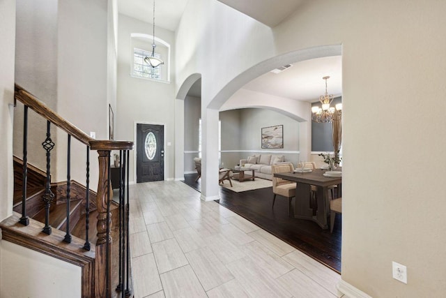 entryway featuring wood finish floors, arched walkways, an inviting chandelier, baseboards, and stairs