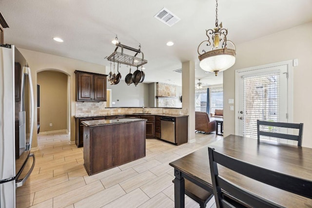 kitchen with dark brown cabinetry, arched walkways, appliances with stainless steel finishes, a center island, and visible vents