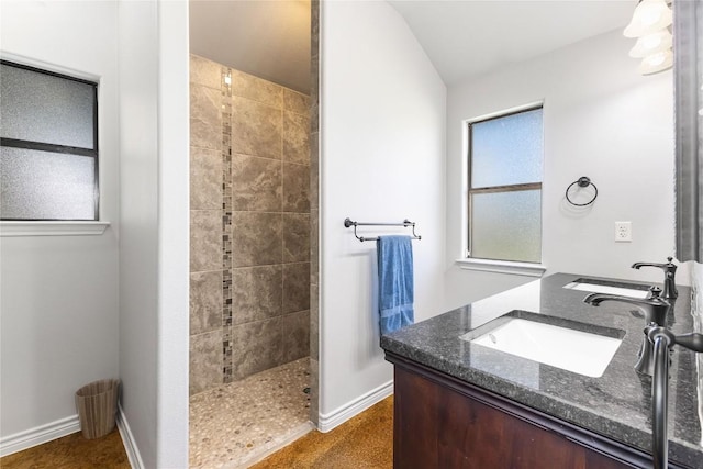 bathroom with double vanity, a walk in shower, baseboards, and a sink