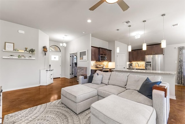 living area with visible vents, baseboards, concrete flooring, and ceiling fan with notable chandelier