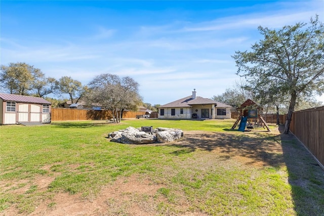 view of yard featuring a fire pit, a playground, a fenced backyard, an outdoor structure, and a storage unit