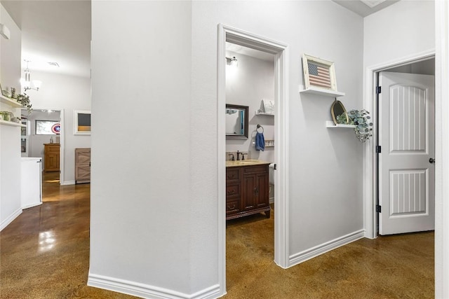 hall featuring an inviting chandelier, baseboards, and a sink