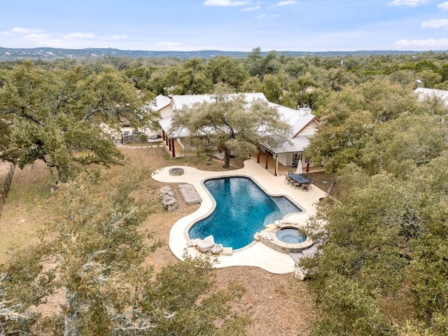 view of swimming pool with a forest view, a fire pit, a pool with connected hot tub, and a patio area