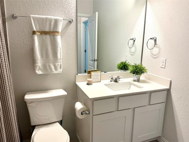 bathroom with toilet, vanity, and a textured wall