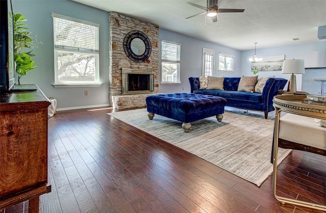 living room with baseboards, a stone fireplace, hardwood / wood-style floors, and ceiling fan with notable chandelier