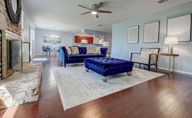 living area with visible vents, a fireplace with raised hearth, ceiling fan with notable chandelier, hardwood / wood-style floors, and baseboards