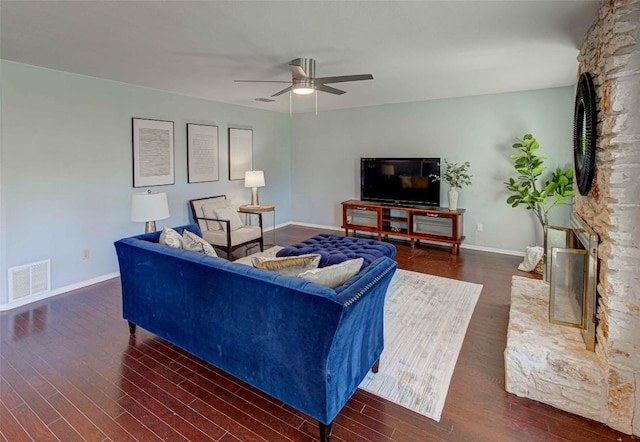 living room with visible vents, ceiling fan, baseboards, a stone fireplace, and wood finished floors