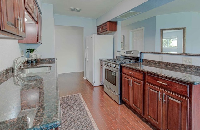 kitchen with visible vents, a sink, dark stone counters, light wood-style floors, and stainless steel range with gas stovetop