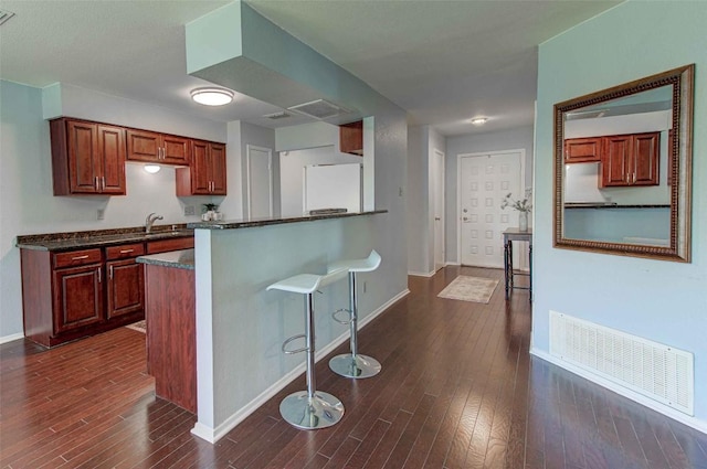 kitchen featuring dark countertops, visible vents, a kitchen bar, freestanding refrigerator, and dark wood-style flooring