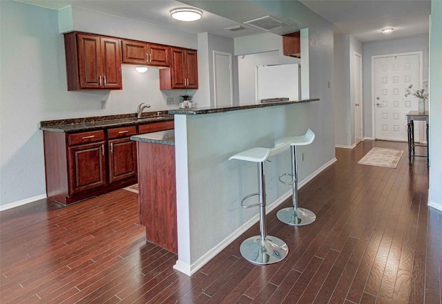 kitchen featuring baseboards, dark wood-style flooring, a kitchen breakfast bar, freestanding refrigerator, and a sink