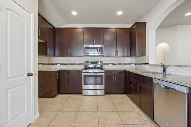 kitchen featuring light stone counters, light tile patterned flooring, stainless steel appliances, and a sink