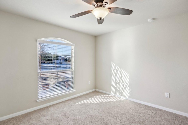 carpeted spare room featuring baseboards and a ceiling fan