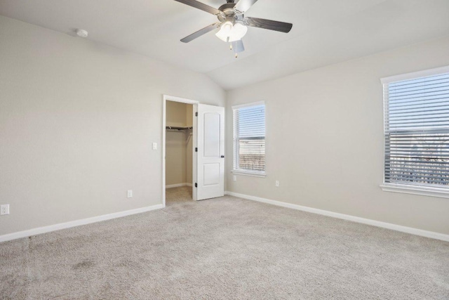 unfurnished bedroom with a walk in closet, vaulted ceiling, baseboards, and light carpet