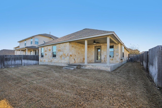 rear view of property featuring a ceiling fan, a yard, a fenced backyard, stone siding, and a patio area