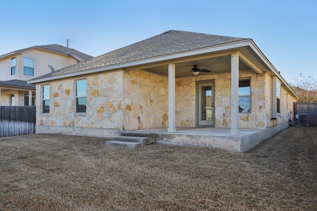 rear view of house featuring stone siding, a ceiling fan, and fence