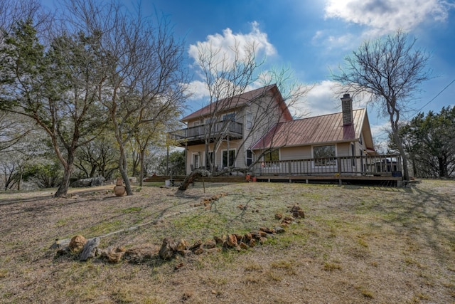 rear view of property featuring a yard, a balcony, a deck, and a chimney