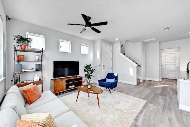 living room with visible vents, baseboards, stairs, light wood-style floors, and a ceiling fan