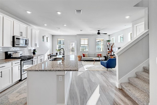 kitchen featuring light stone countertops, decorative backsplash, stainless steel appliances, white cabinetry, and a sink