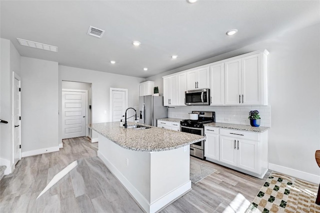 kitchen featuring visible vents, an island with sink, decorative backsplash, appliances with stainless steel finishes, and white cabinetry