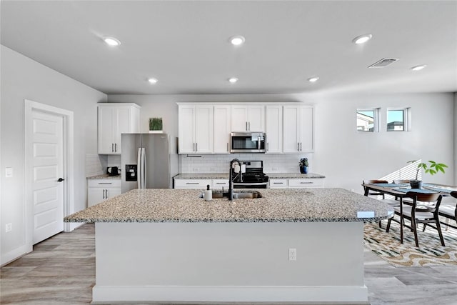 kitchen featuring visible vents, a center island with sink, light stone counters, stainless steel appliances, and white cabinets