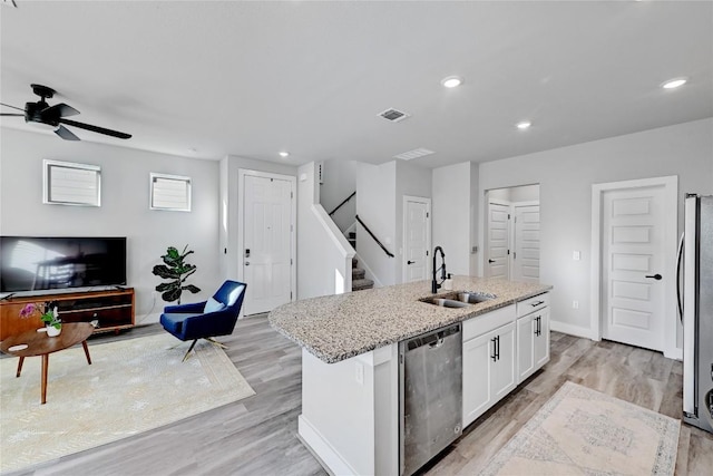 kitchen with a sink, light stone counters, open floor plan, stainless steel appliances, and white cabinets