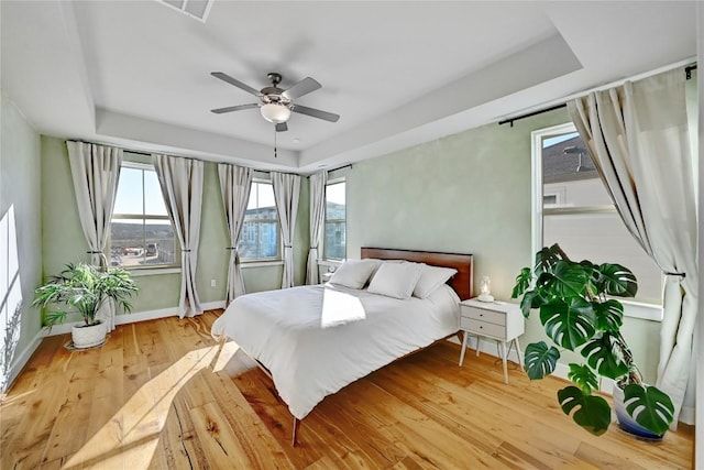 bedroom featuring a tray ceiling, baseboards, ceiling fan, and light wood finished floors