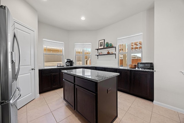 kitchen featuring a center island, baseboards, light stone countertops, light tile patterned floors, and stainless steel refrigerator with ice dispenser