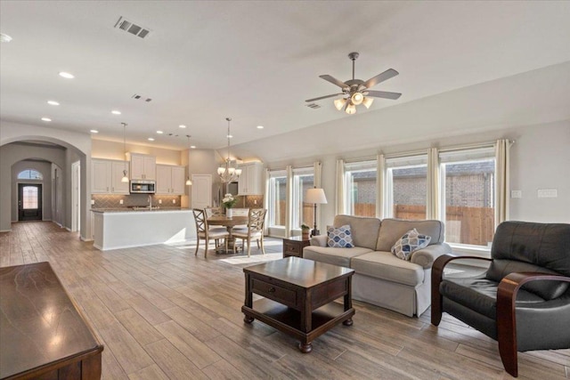 living room featuring visible vents, light wood-style flooring, ceiling fan with notable chandelier, recessed lighting, and arched walkways