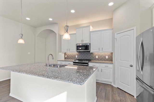 kitchen featuring dark wood-type flooring, a sink, tasteful backsplash, stainless steel appliances, and arched walkways