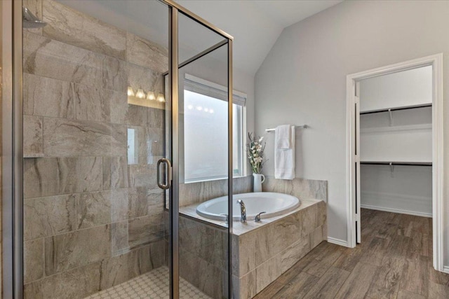 bathroom with a spacious closet, a garden tub, vaulted ceiling, a stall shower, and wood finished floors