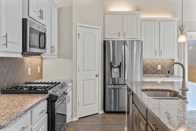 kitchen with dark wood-type flooring, a sink, appliances with stainless steel finishes, white cabinets, and light stone countertops