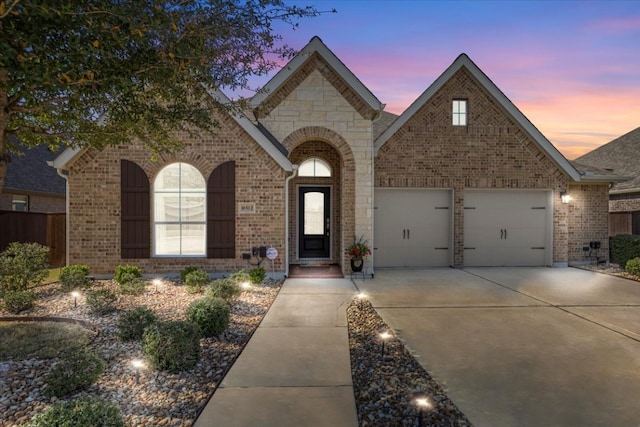 french country style house with concrete driveway, an attached garage, and brick siding