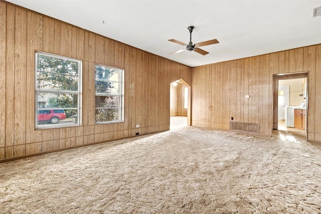 carpeted empty room featuring visible vents, a ceiling fan, washer / clothes dryer, arched walkways, and wooden walls