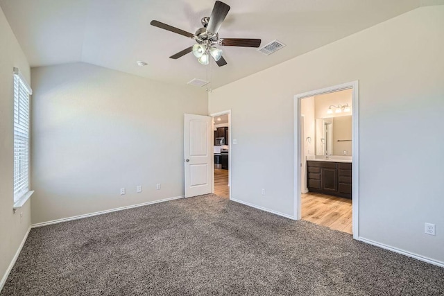 unfurnished bedroom featuring visible vents, light carpet, ensuite bathroom, baseboards, and vaulted ceiling