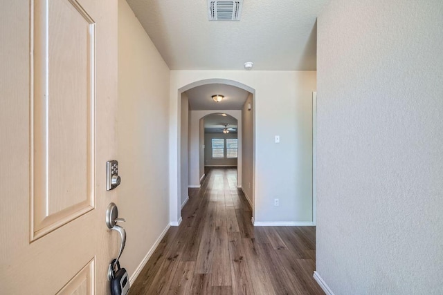 corridor featuring wood finished floors, visible vents, baseboards, arched walkways, and a textured ceiling