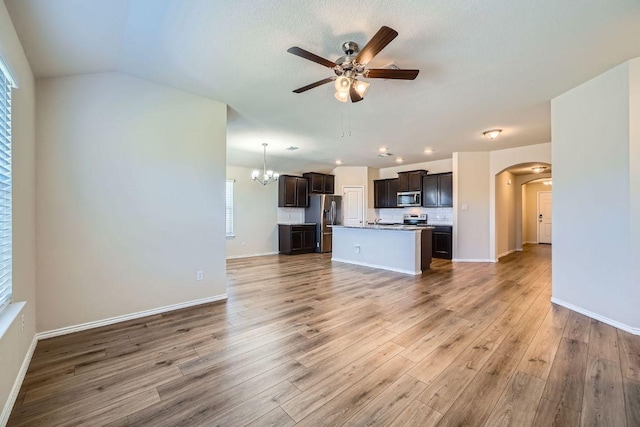 unfurnished living room with arched walkways, ceiling fan with notable chandelier, baseboards, and wood finished floors