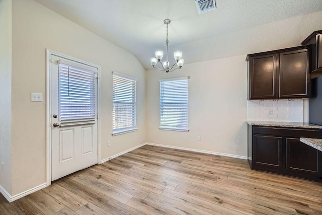 unfurnished dining area with visible vents, baseboards, light wood-type flooring, vaulted ceiling, and an inviting chandelier