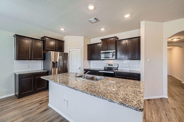 kitchen featuring visible vents, light wood finished floors, arched walkways, a sink, and stainless steel appliances