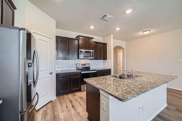 kitchen with visible vents, arched walkways, a sink, stainless steel appliances, and light wood-style floors