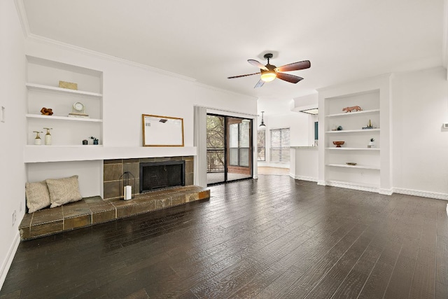 unfurnished living room featuring built in shelves, ceiling fan, baseboards, a tiled fireplace, and dark wood-style floors