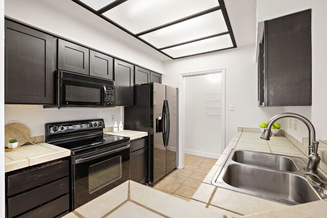 kitchen featuring light tile patterned floors, tile countertops, black appliances, and a sink