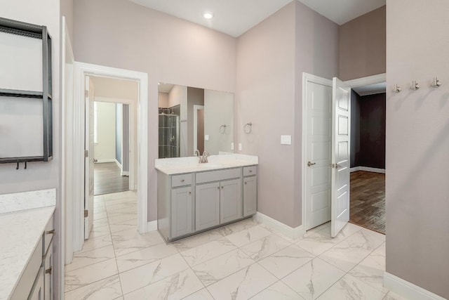 bathroom with marble finish floor, a high ceiling, a shower stall, baseboards, and vanity