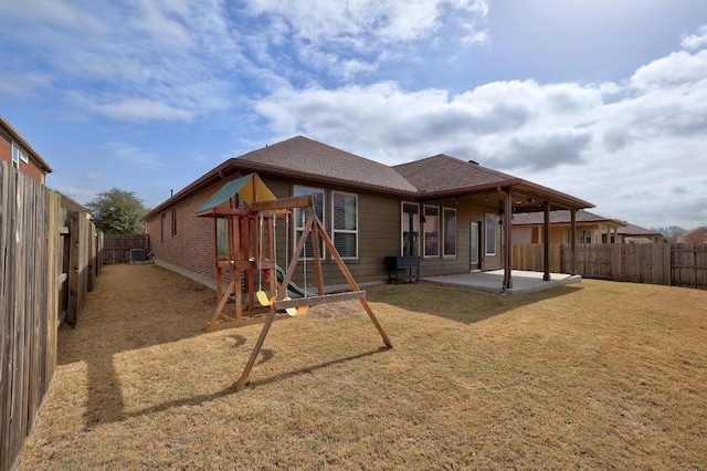 back of property featuring a yard, a fenced backyard, a shingled roof, a playground, and a patio area