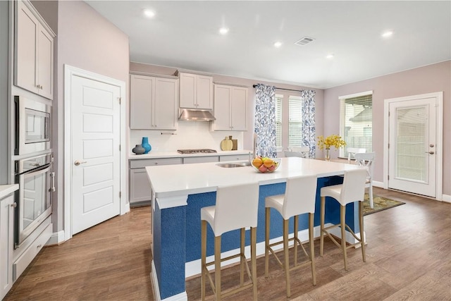 kitchen with wood finished floors, visible vents, stainless steel appliances, light countertops, and under cabinet range hood