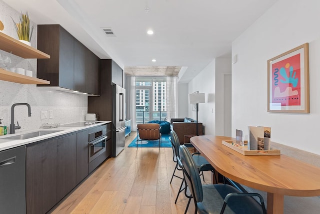 kitchen featuring light wood-type flooring, open shelves, stainless steel appliances, a sink, and tasteful backsplash