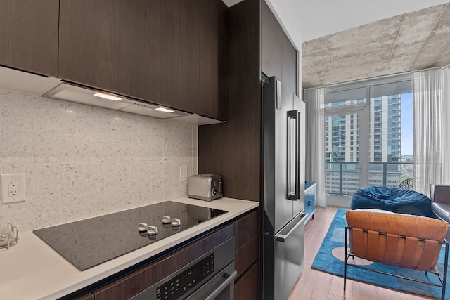 kitchen featuring light wood-style flooring, high end fridge, dark brown cabinets, black electric cooktop, and tasteful backsplash