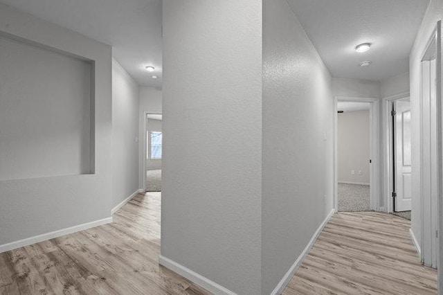 hallway featuring baseboards, wood finished floors, and a textured wall