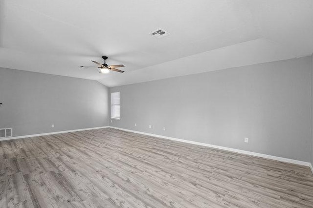 empty room with visible vents, wood finished floors, baseboards, ceiling fan, and vaulted ceiling