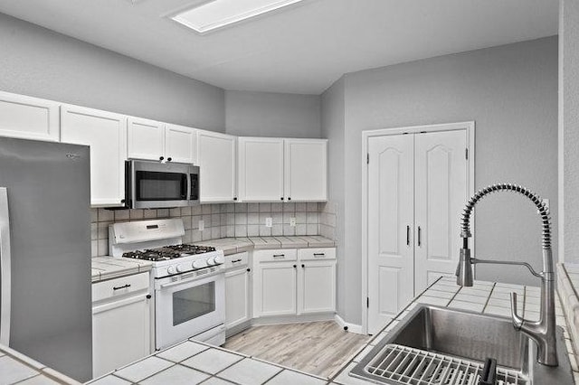 kitchen featuring a sink, appliances with stainless steel finishes, tile counters, and white cabinets